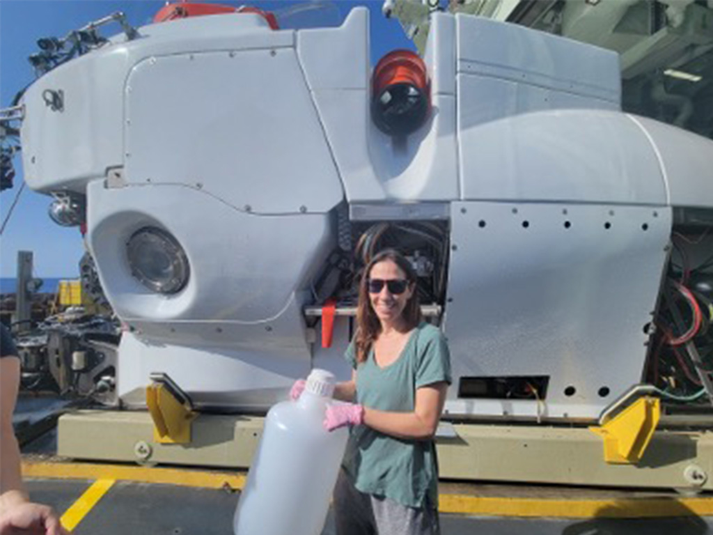 Olivia Nigro standing in front of the Alvin submarine, aboard the R/V Atlantis.
