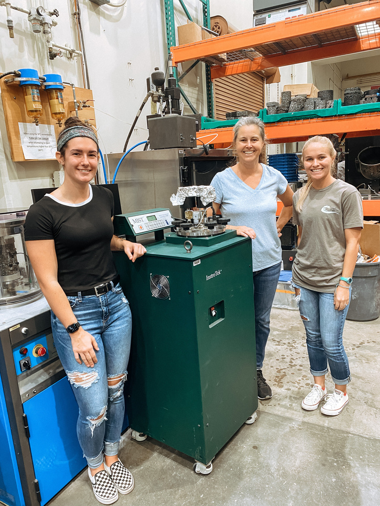 HPU CMDR team members Cara Megill (HPU MSMS ‘23), Jennifer Lynch, Ph.D., and Raquel Corniuk are pictured by the Moisture Induced Stressed Tester at UH’s Pavement Engineering Laboratory. An asphalt sample is loaded into its water bath, and it applies heat and pressure to the asphalt sample to weather it.