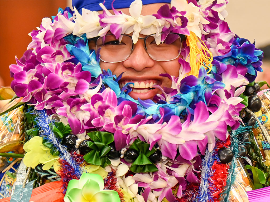 An HPU graduate celebrates, wearing leis given by family and friends