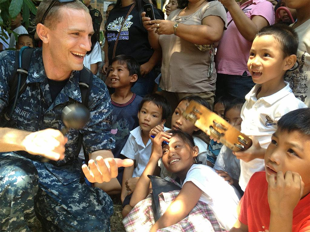 Zach Drury (left) shares a song and a smile with local children during a visit in Southeast Asia