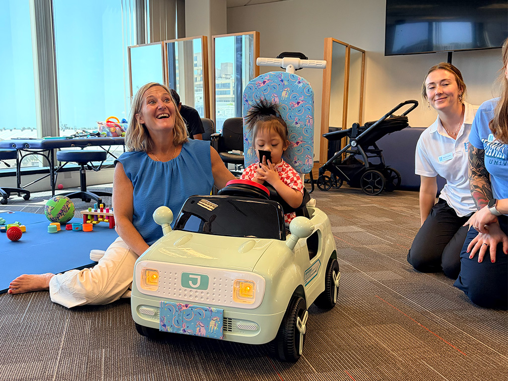 A child getting ready to take off and explore the laboratory floor on her new ride-on car