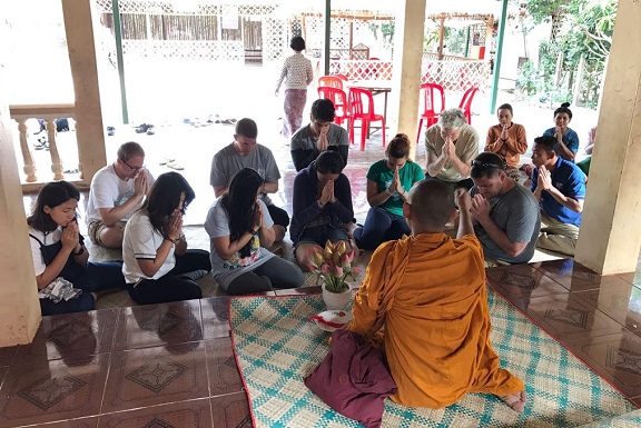 Group of students and a monk praying in a Cambodian temple